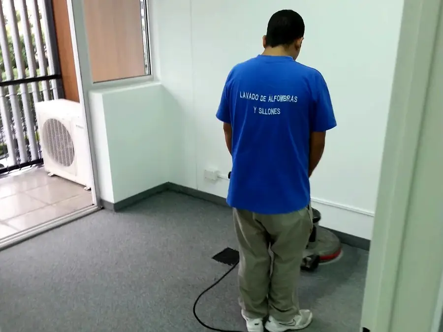 Operario de Carpet Clean lavando una alfombra con máquina rotativa en una oficina