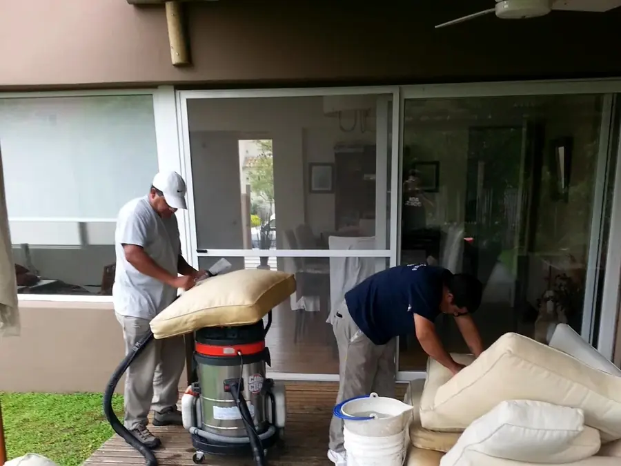 Dos operarios de Carpet Clean lavando almohadones de sillones en una galería